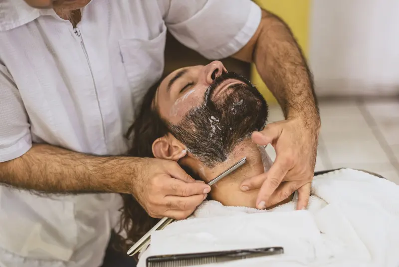 Barbero afeitando con navaja a un cliente reclinado