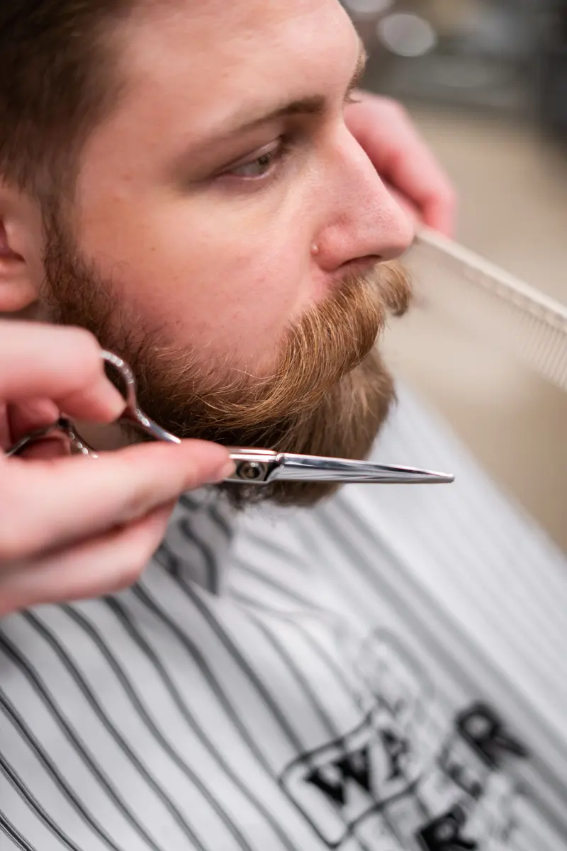 Barbero perfilando con tijera y peine la barba de un cliente