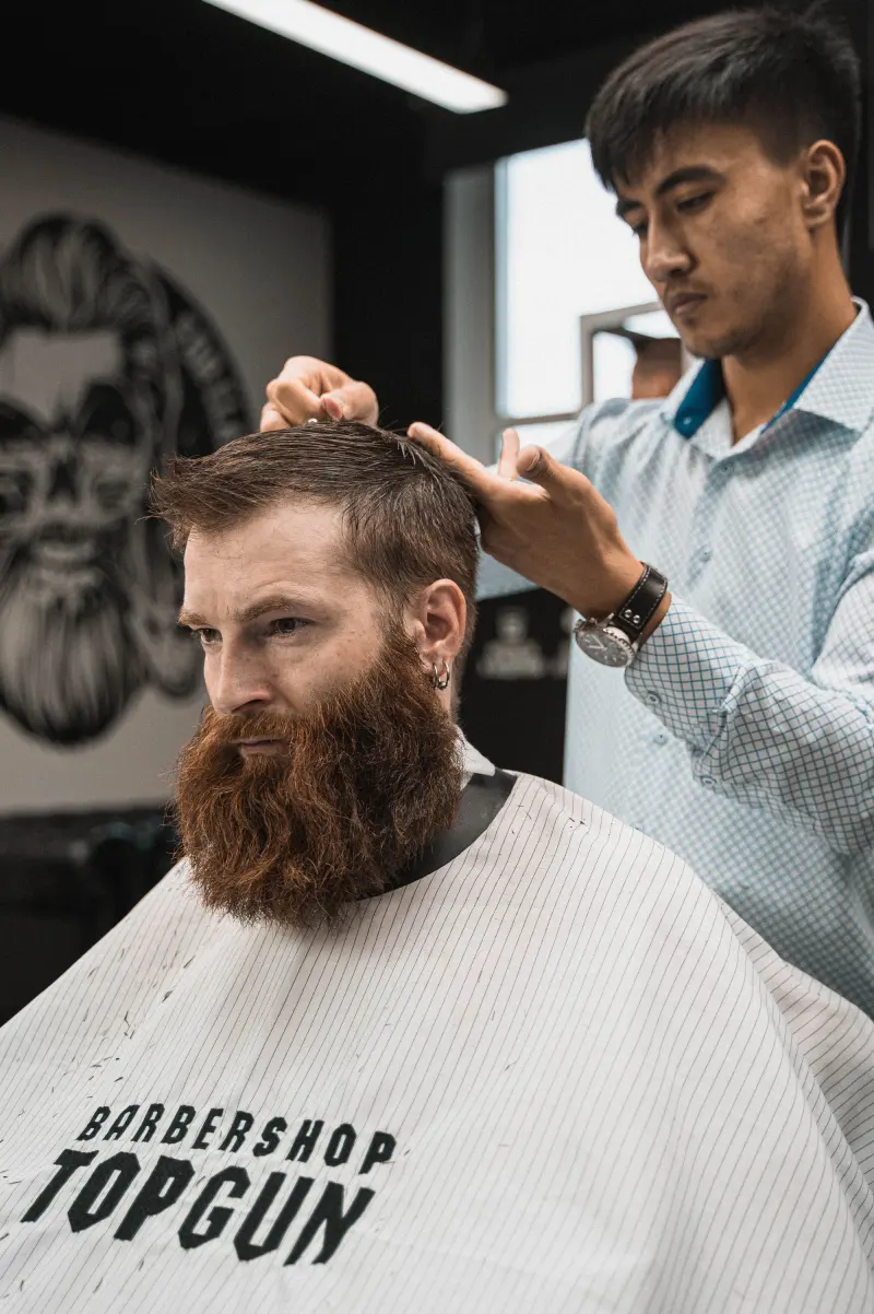 Barbero cortando a tijera el pelo de un cliente con barba